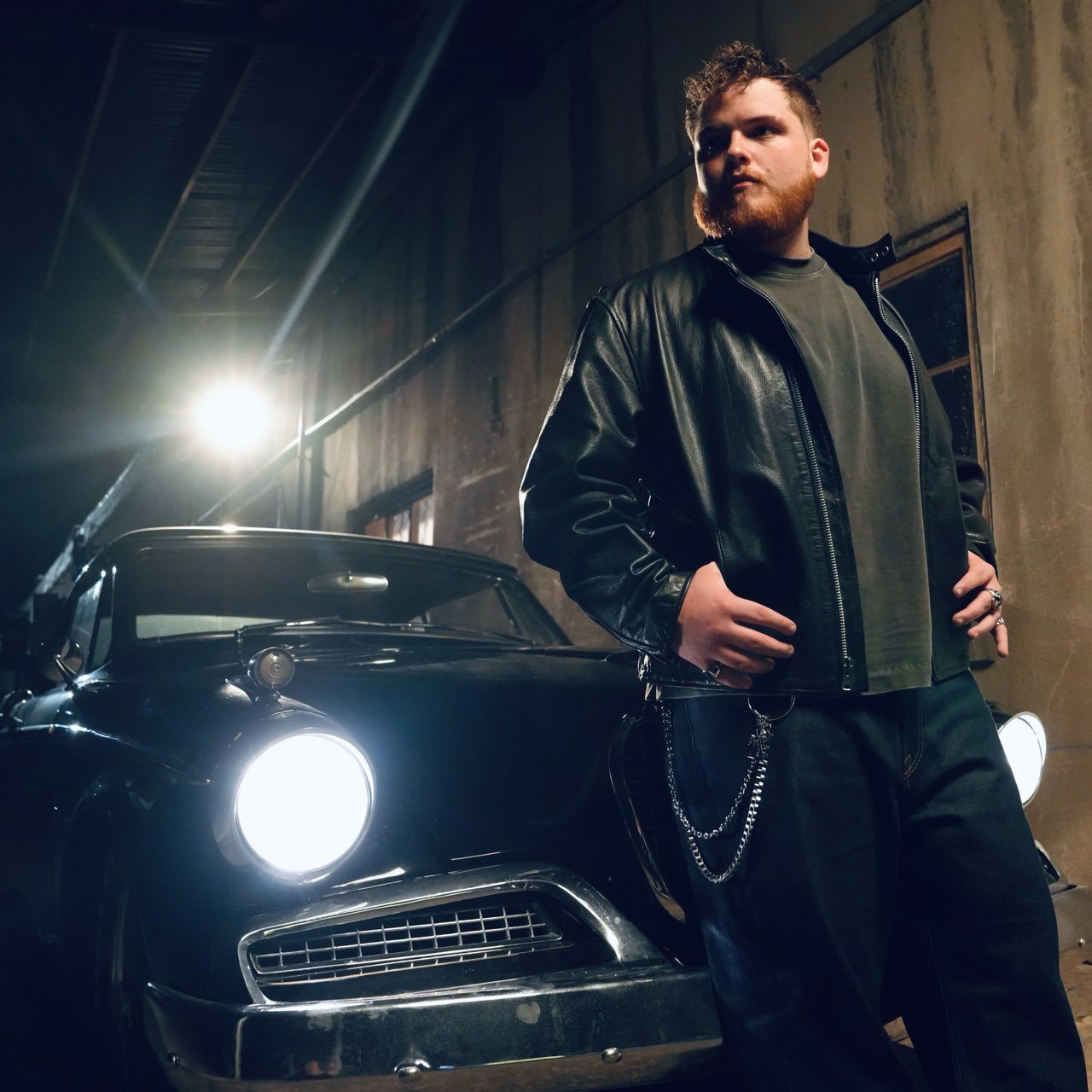 Tanner Castille leaning against a vintage black car with its headlights on