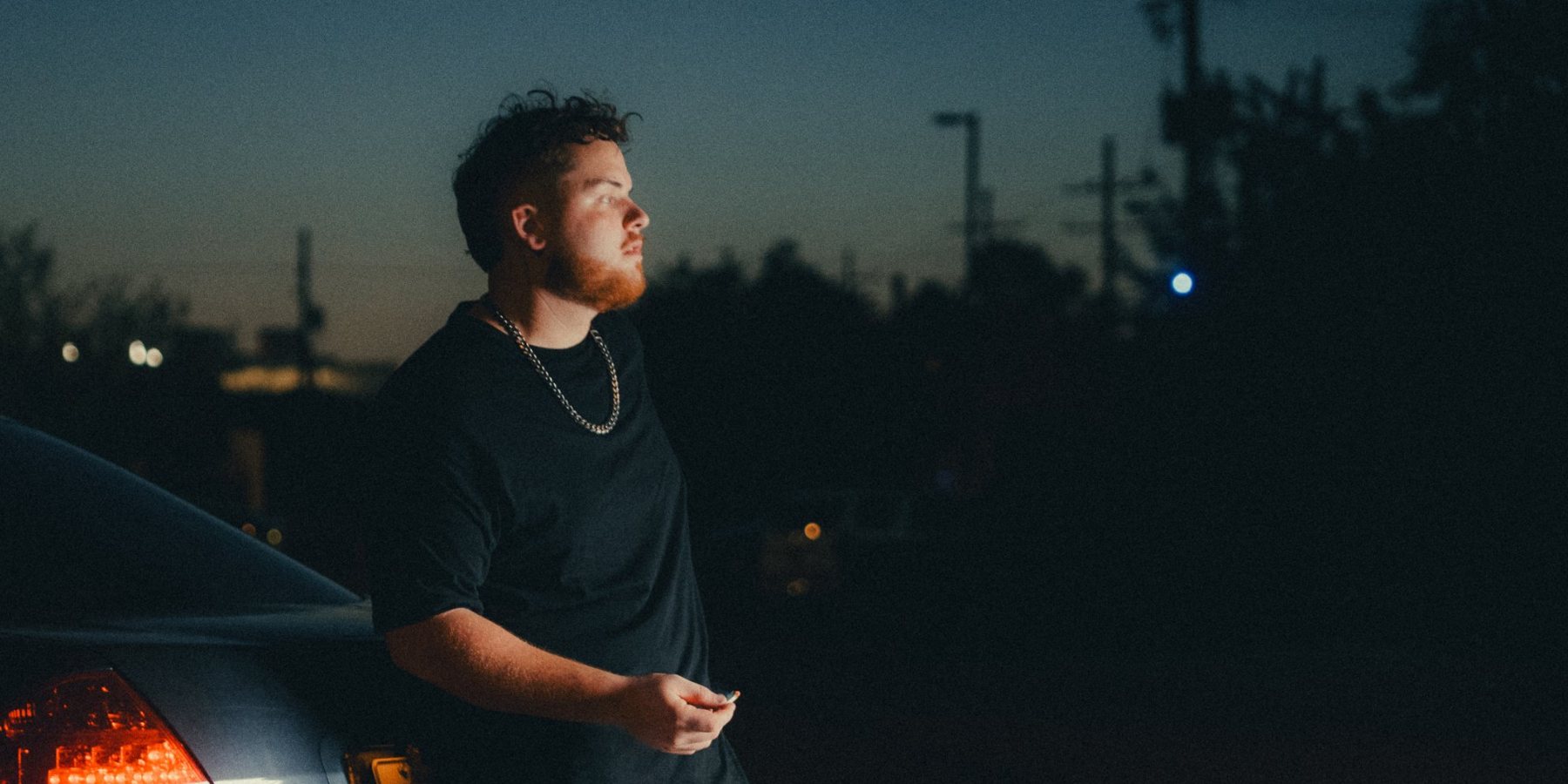 Tanner Castille leaning on a car at dusk, taillight glowing red